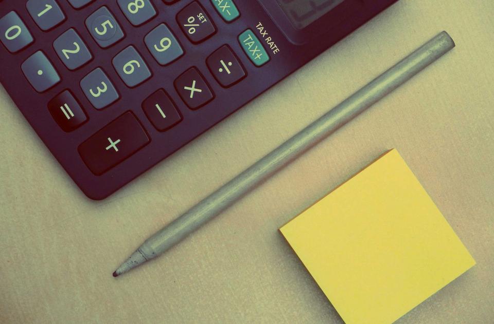 A calculator, pencil, and blank sticky note on a desk, ready for figuring costs.
